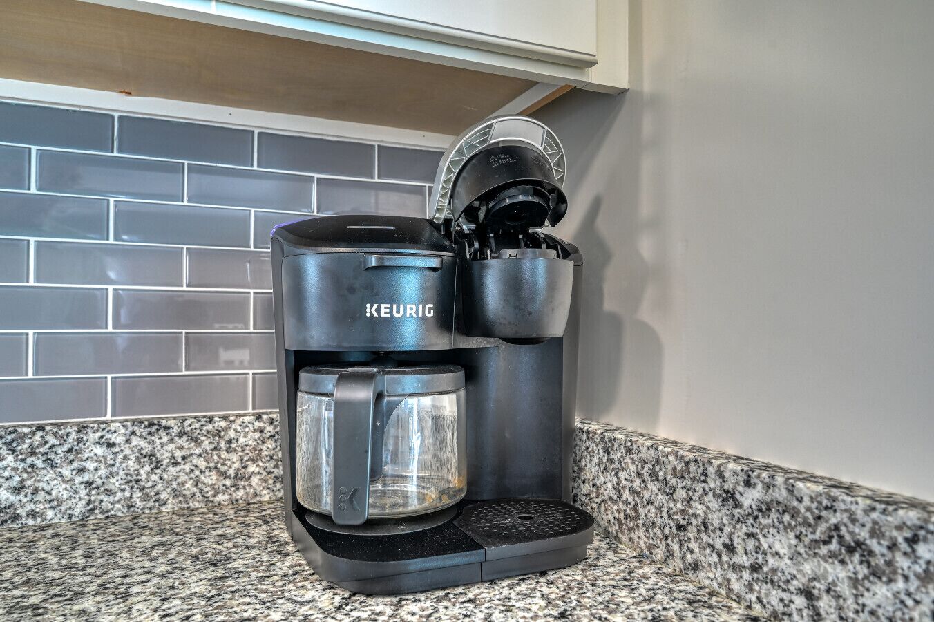A Keurig coffee maker on a granite countertop with a tiled backsplash.