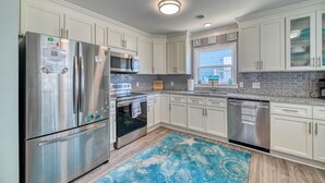 Een moderne keuken met roestvrijstalen apparatuur, witte kasten en een blauw tapijt met een patroon.