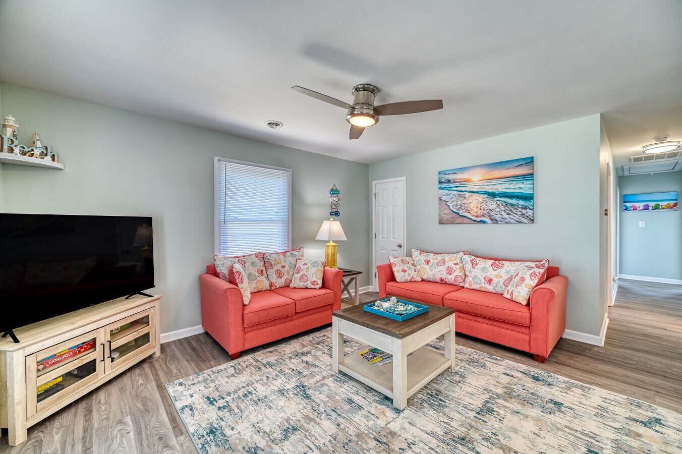A living room with two red sofas, a coffee table, a TV, and a painting of a beach scene.
