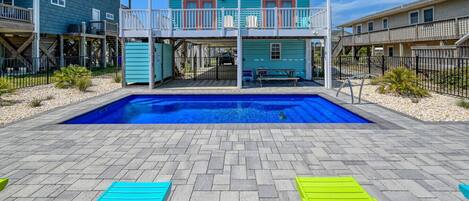 A pool area with a turquoise house, a wooden deck, and two benches.