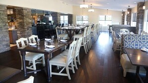 A spacious dining area with long tables and chairs, stone accents on the walls, and a kitchen area visible in the background.