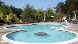 A circular pool with a central hot tub, surrounded by lounge chairs and umbrellas.