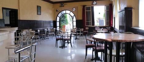 A spacious dining area with multiple tables and chairs, a large arched window, and a view of greenery outside.
