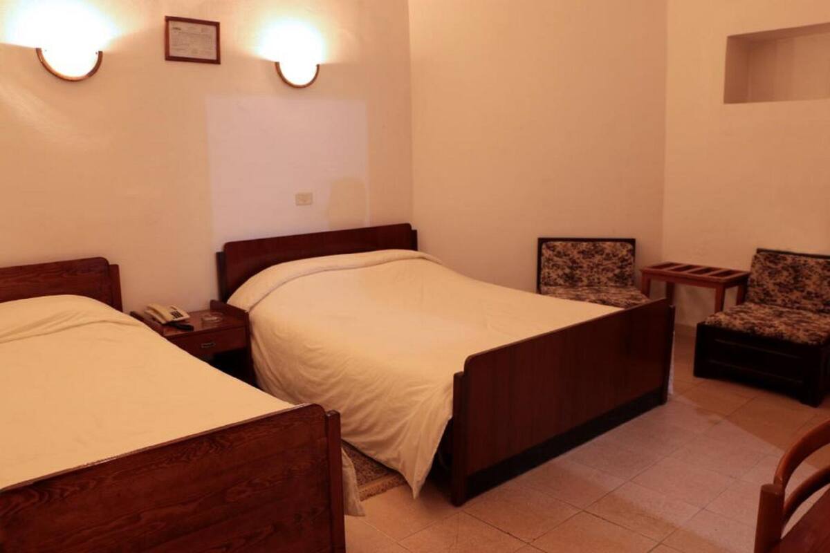 A hotel room with two wooden beds, a small side table with a telephone, and a patterned armchair.