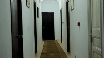 Un pasillo estrecho con paredes blancas, una puerta oscura al final y una alfombra marrón.