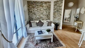 A living room with a white sofa, a coffee table, a patterned rug, and a stone wall. - M318 - Marcelli, new comfortable three-room apartment by the sea (Marcelli)