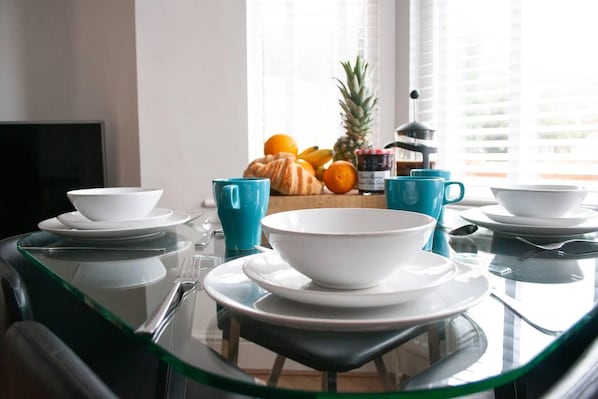 A dining table set with white plates, blue cups, and a large bowl. - Apartment Ideal for Hospital by Nest Stays (Bedford)