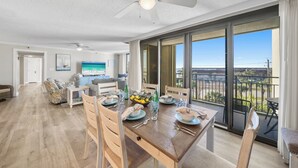 Un comedor amplio con una gran mesa dispuesta para seis comensales, sillas de madera y vista al océano a través de amplias puertas correderas de vidrio.