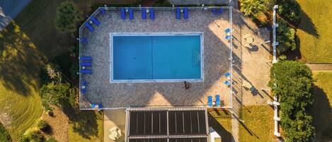 Vue aérienne d’une piscine rectangulaire entourée d’une terrasse carrelée, agrémentée de chaises longues bleues et d’un ensemble de panneaux solaires.
