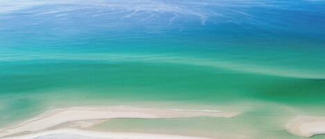 An aerial view of a beach with clear turquoise waters and a sandy shoreline.