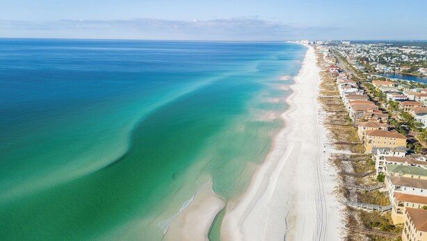 Vista aérea de una zona costera con una extensa playa de arena, edificios residenciales cercanos y una vista despejada del océano.
