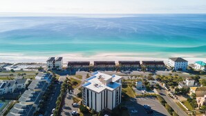 Un hotel costero con varias edificaciones, un estacionamiento y una playa al fondo.