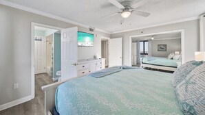 Un dormitorio con cama, ventilador de techo, televisión y baño visible a través de una puerta abierta.