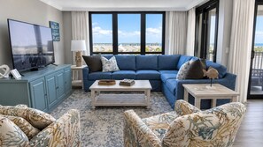 Un salon avec un canapé bleu, un téléviseur, une table basse et une vue sur la plage.