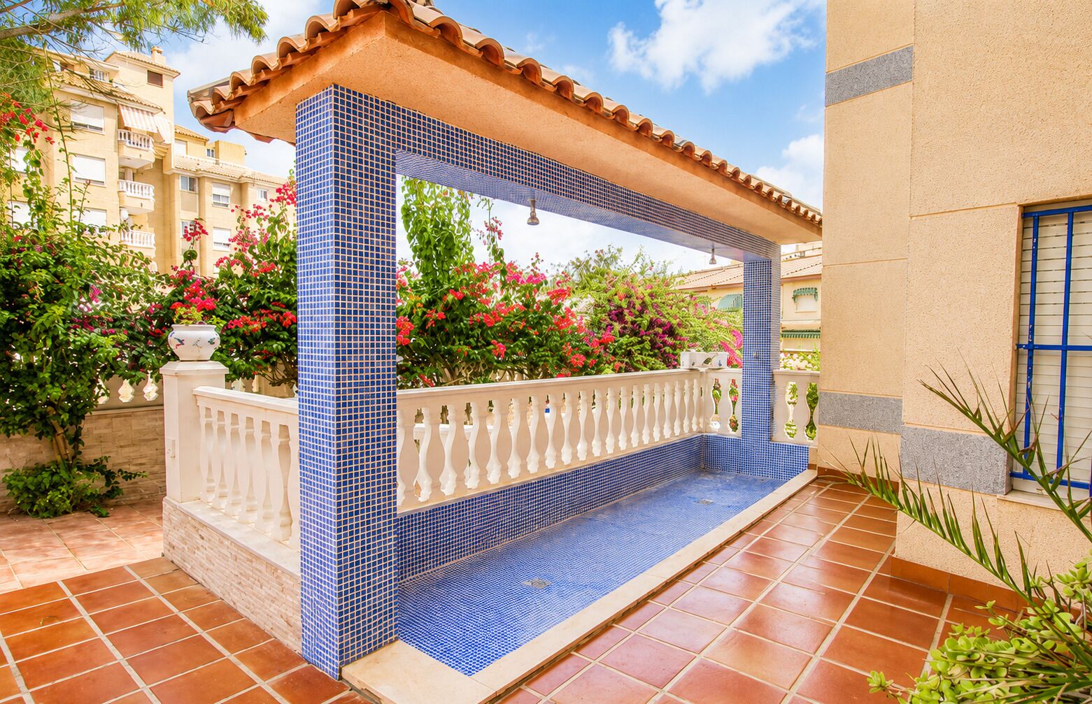 Un espacio exterior cubierto con piso de baldosas, baranda blanca y pared de baldosas con un diseño azul.