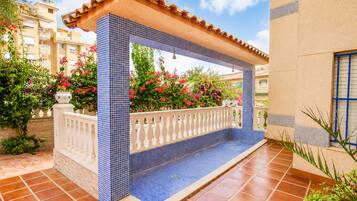 Un espacio exterior cubierto con piso de baldosas, baranda blanca y pared de baldosas con un diseño azul.
