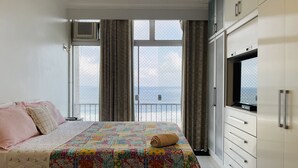 A bedroom with a bed, a TV, and a view of the sea. - Frente Mar Encantador (Rio de Janeiro)