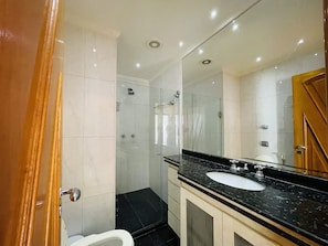 Ein modernes Badezimmer mit einer gläsernen Duschkabine, einer weißen Toilette und einem schwarzen Marmorwaschbecken.