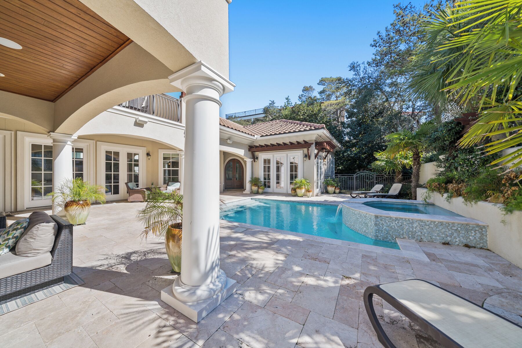 A pool area with a tiled deck, lounge chairs, and potted plants.