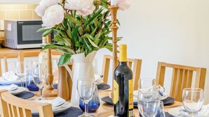 Una mesa de comedor dispuesta con platos, vasos y una botella de vino, con un florero de flores y velas.
