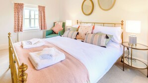 Una cama bien hecha con almohadas y una toalla doblada, un sillón verde, una mesa redonda con una lámpara y dos espejos en la pared.