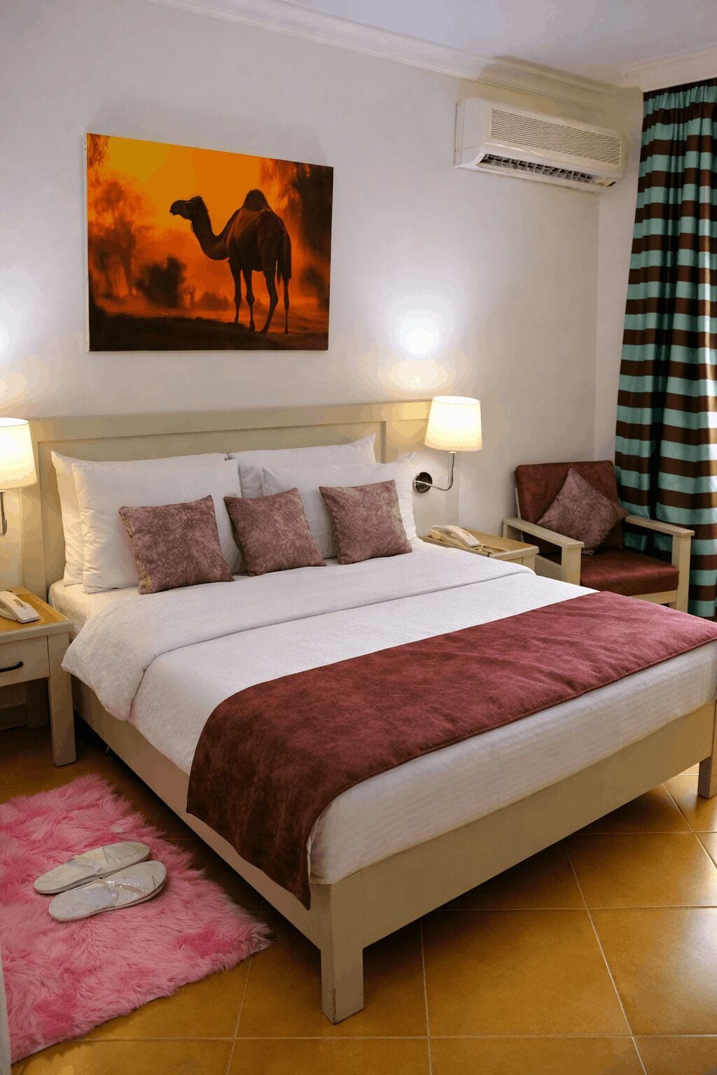 A bed with a white headboard, a red throw blanket, and a pink furry rug.