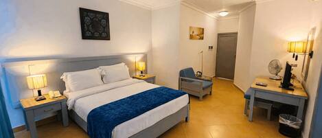 A hotel room with a bed, bedside lamps, a desk with a computer, a chair, and a small table.