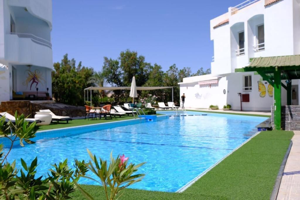 A swimming pool with lounge chairs, a covered seating area, and a building with a mural.