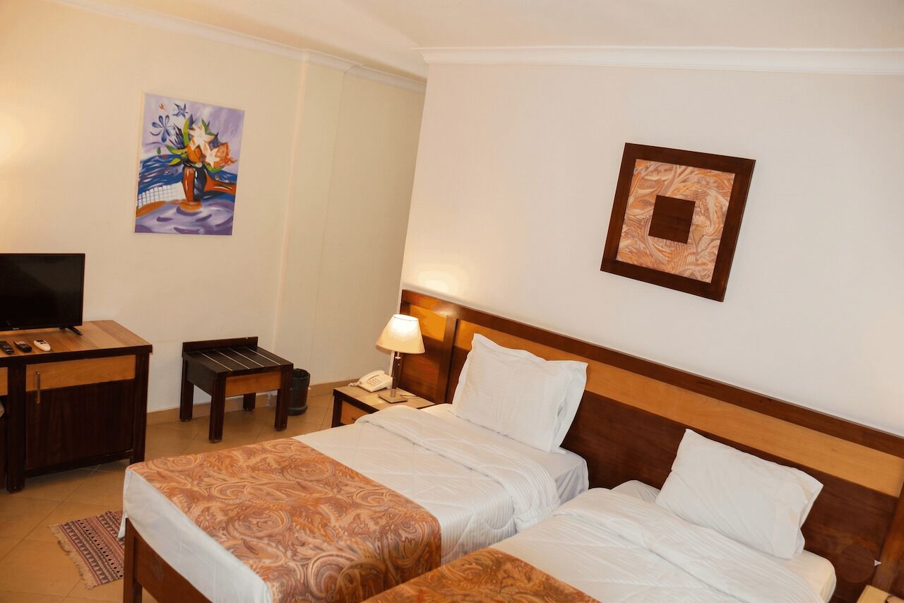 A hotel room with two beds, a desk with a TV, a lamp, and a painting on the wall.