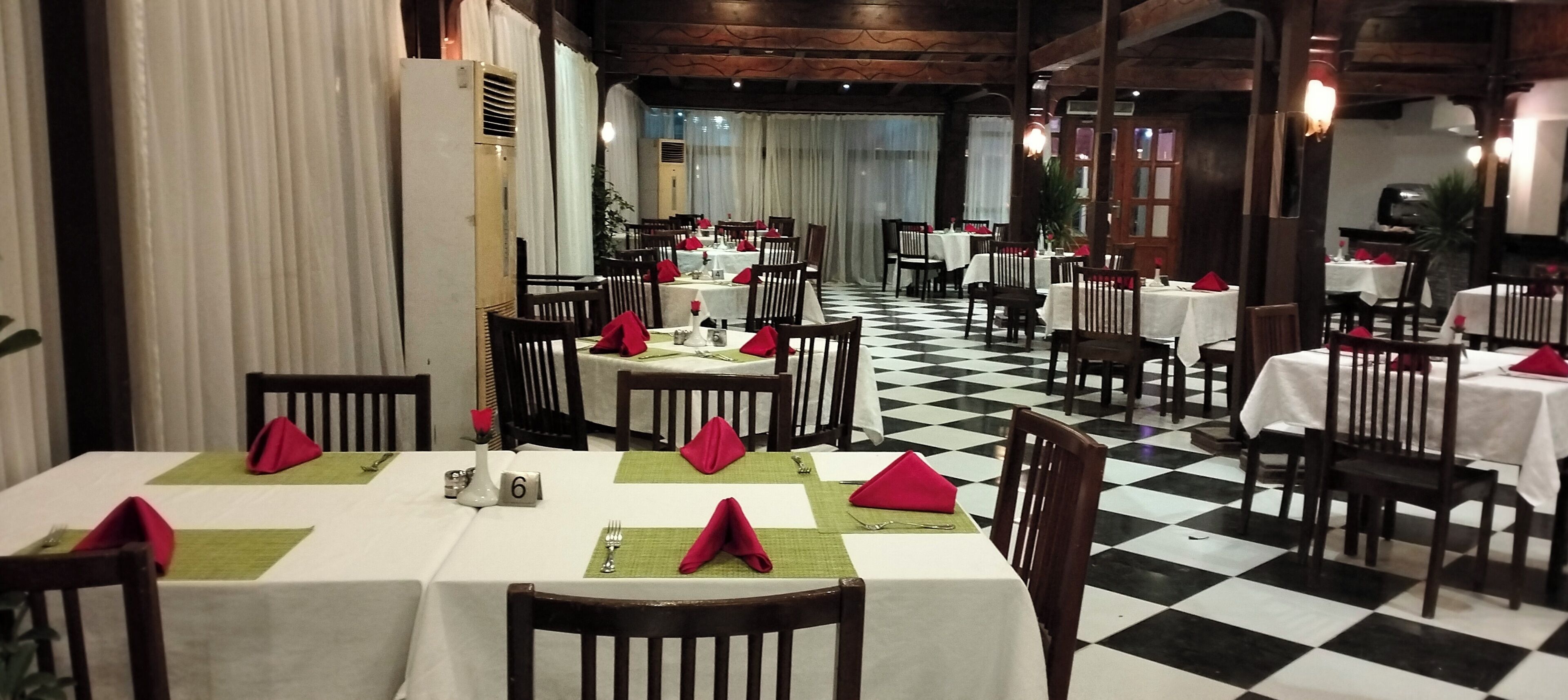 A restaurant with checkered flooring, tables set with red napkins, and a checkered ceiling.