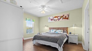 Une chambre à coucher avec un lit, des tables de chevet, un ventilateur de plafond et des œuvres d’art accrochées au mur.