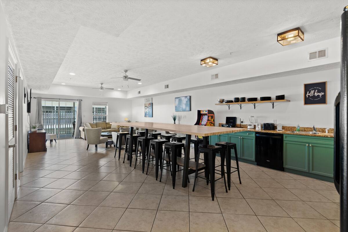 A spacious kitchen with a long island, bar stools, and green cabinets.