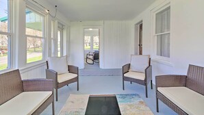 A covered patio area with wicker furniture and large windows. - Walk to Beach! Sodus Point Escape w/ Private Yard (Sodus Point)