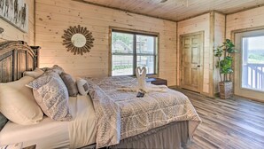 Une chambre dans une cabane en bois, avec un lit, un ventilateur de plafond, une fenêtre et une porte.
