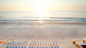 A beach view with sunlit sand and a row of blue lounge chairs.