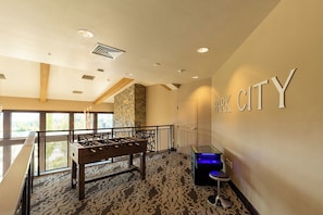 Um saguão de hotel com mesa de pebolim, mesa de bilhar e uma placa na parede com a inscrição 'PARK CITY'.