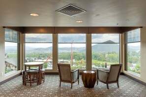 A room with large windows, a round table, two chairs, and a decorative vase.