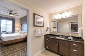 A hotel room with a bed, a bathroom with a sink and mirror, and a ceiling fan.
