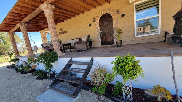 Un patio cubierto con mobiliario exterior, un arco de piedra y una variedad de plantas en macetas.