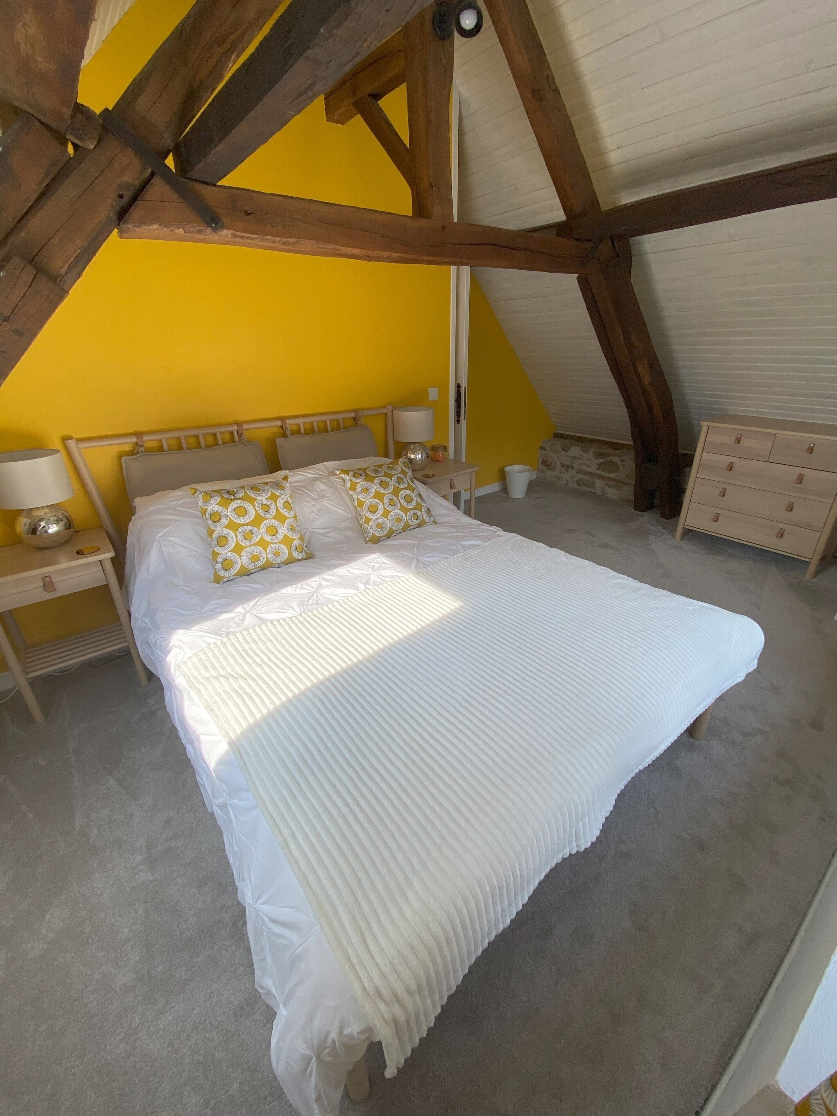 A bedroom with a bed, nightstands, a dresser, and a sloped ceiling.