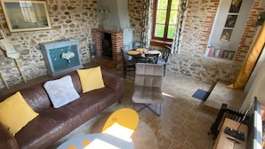 Ein gemütliches Wohnzimmer mit Steinwand, Kamin, Ledersofa, rundem Couchtisch und Essbereich mit Tisch und Stühlen.