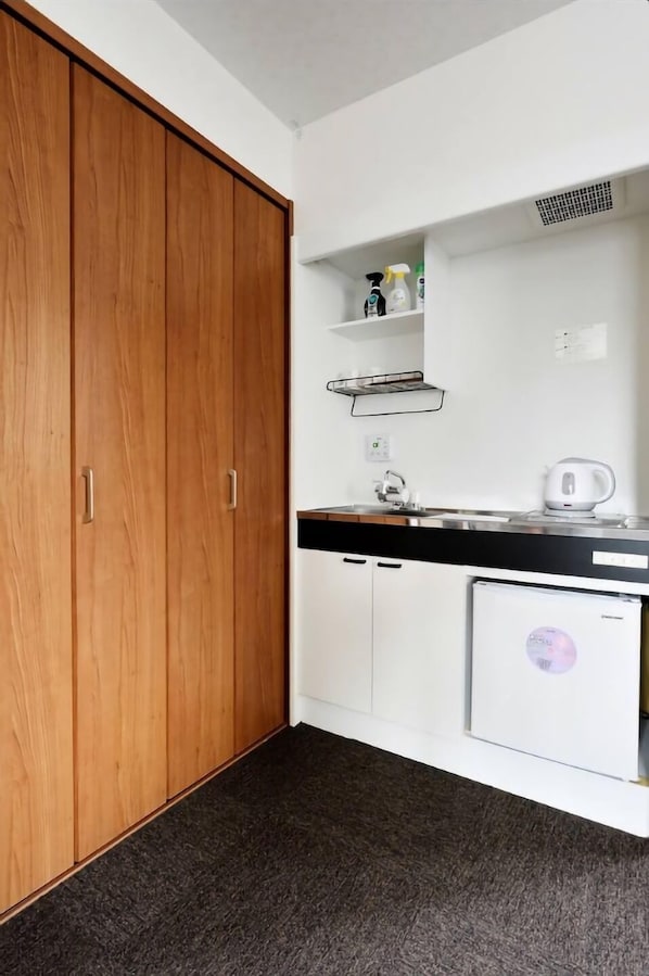 A kitchen with a wooden wardrobe, white cabinets, a black countertop, a kettle, and a refrigerator.