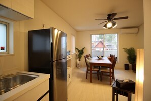 A modern kitchen with a stainless steel refrigerator, a dining area with wooden chairs, and a ceiling fan.