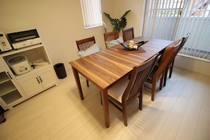 A dining area with a wooden table and chairs, a microwave, a small refrigerator, and a potted plant.