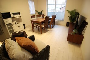 A living room with a dining table, chairs, a sofa, a TV, and a plant.