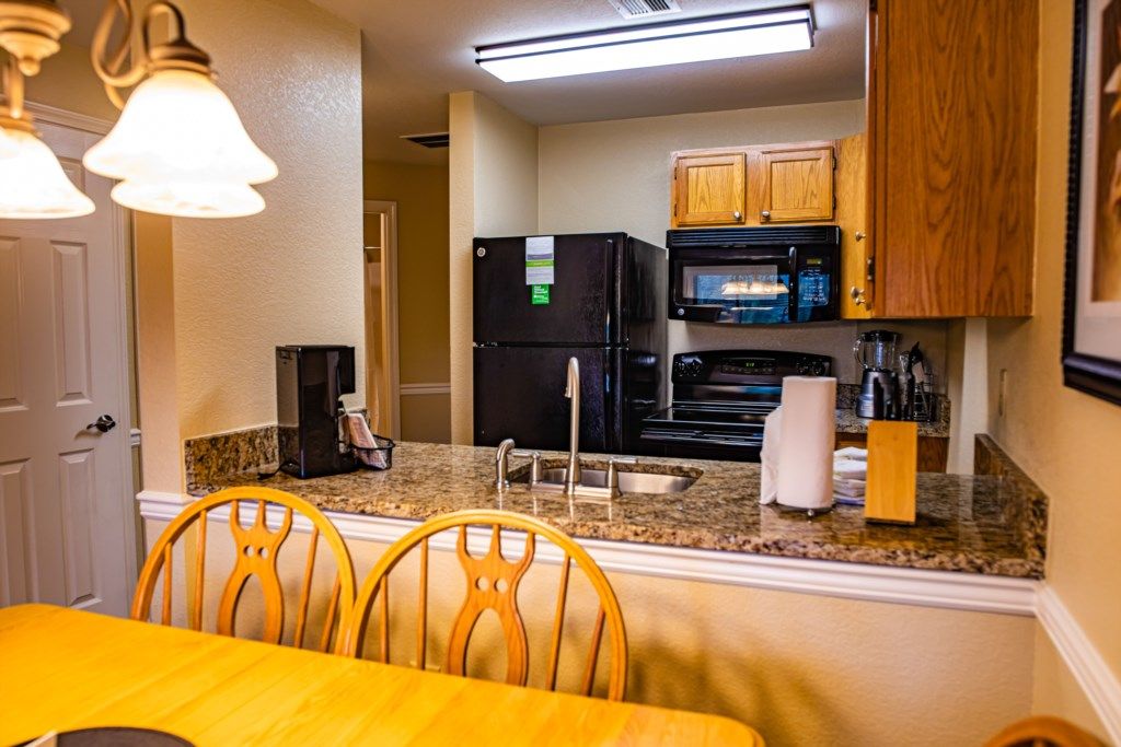 A compact kitchen with a refrigerator, microwave, and sink. There are wooden cabinets and a granite countertop.