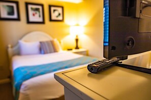 A hotel room with a bed, a bedside table with a remote control, and a lamp. - Pigeon Forge | Friends' Outdoor Escape | Hiking + Pool | 2BR Townhome (Pigeon Forge)