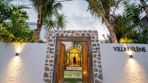 A villa entrance with a stone wall, wooden doors, and a pool area visible through the archway. - Tropical villa style • Sleeps six • Berawa (Kecamatan Kuta Utara)