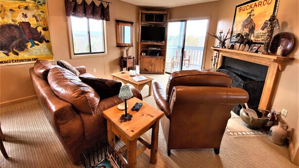 A living room with a leather sofa, a wooden coffee table, and a fireplace. There is a large window and a door leading to a balcony. - BR260 Perfect for 2 couples! Close to Towns. (Davis)