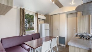 A compact kitchenette with a gas stove, a refrigerator, and a window with curtains.